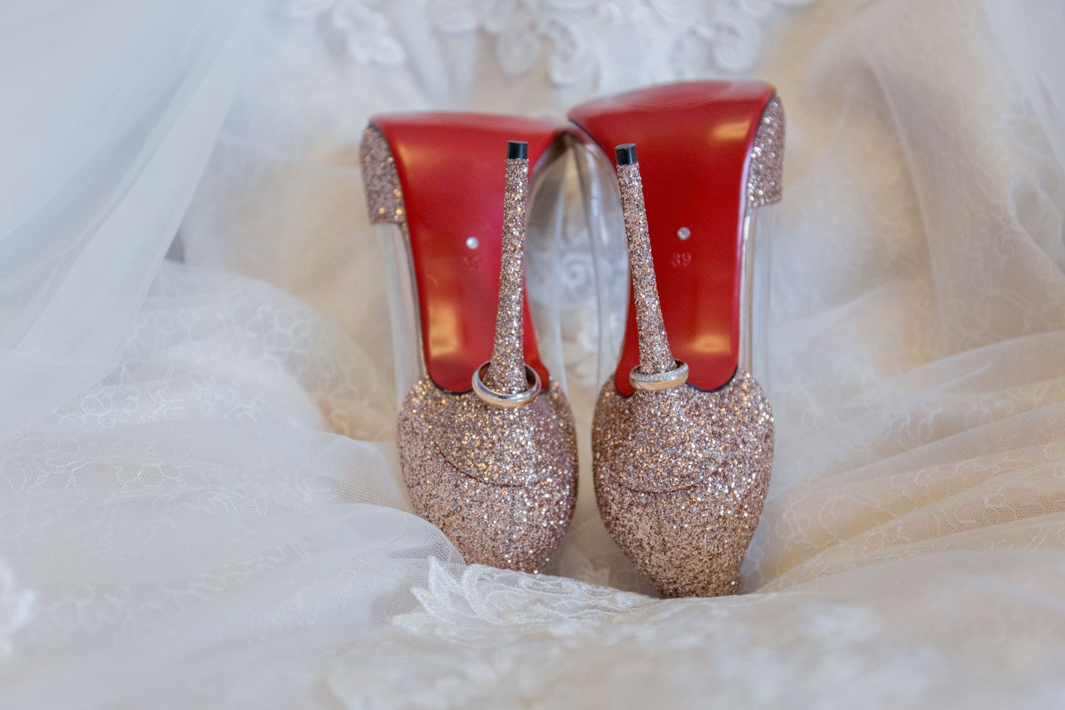 Glittery gold Christian Louboutin wedding heels with red soles displayed on white bridal gown fabric.