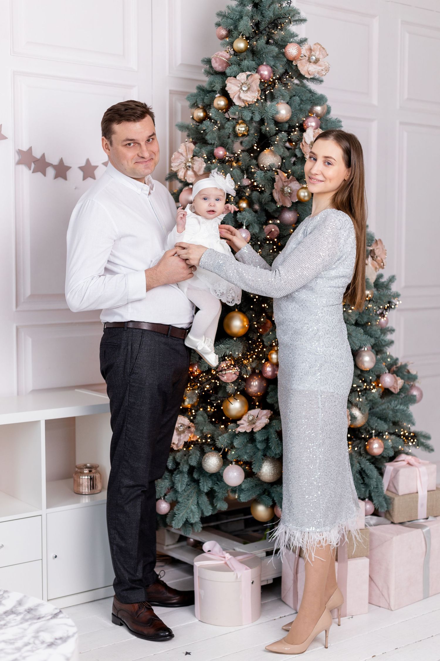 Festive family photos against white wall with decorated Christmas tree and pink gift boxes.