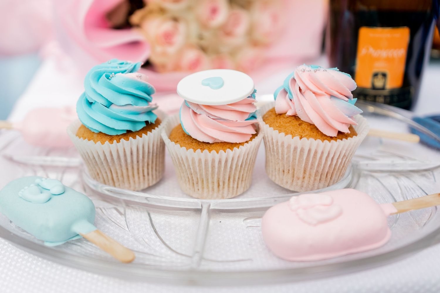 Three decorated cupcakes with blue and pink swirled frosting on a white cake stand.