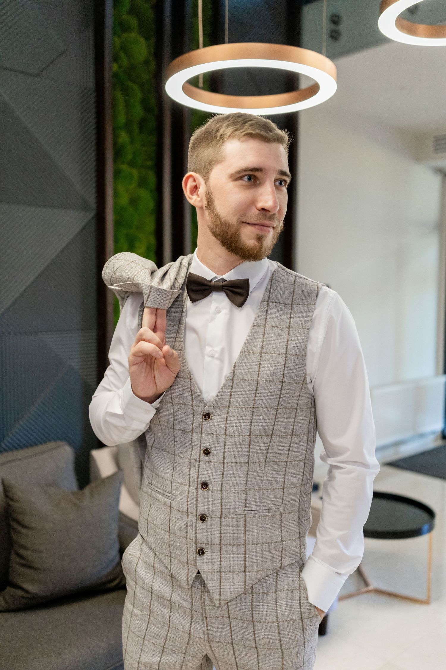 A groom in a checkered vest and white shirt poses playfully.
