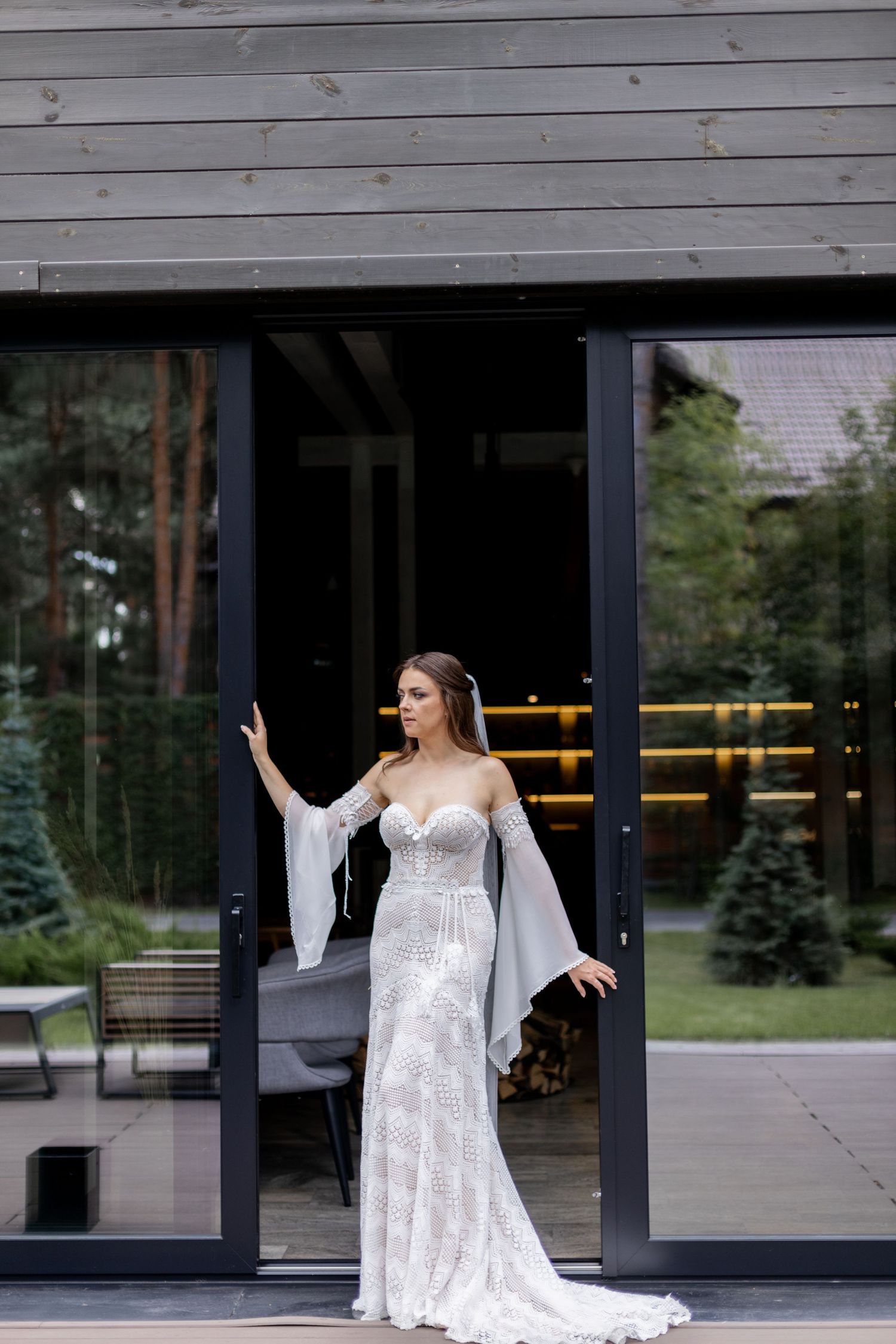 Bride in fitted lace wedding dress poses elegantly in modern doorframe.