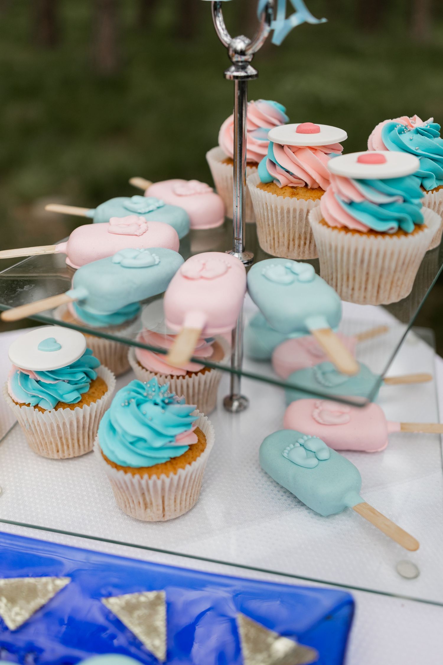 Cupcakes and popsicle-shaped cookies in pink and blue displayed on a tiered dessert stand.