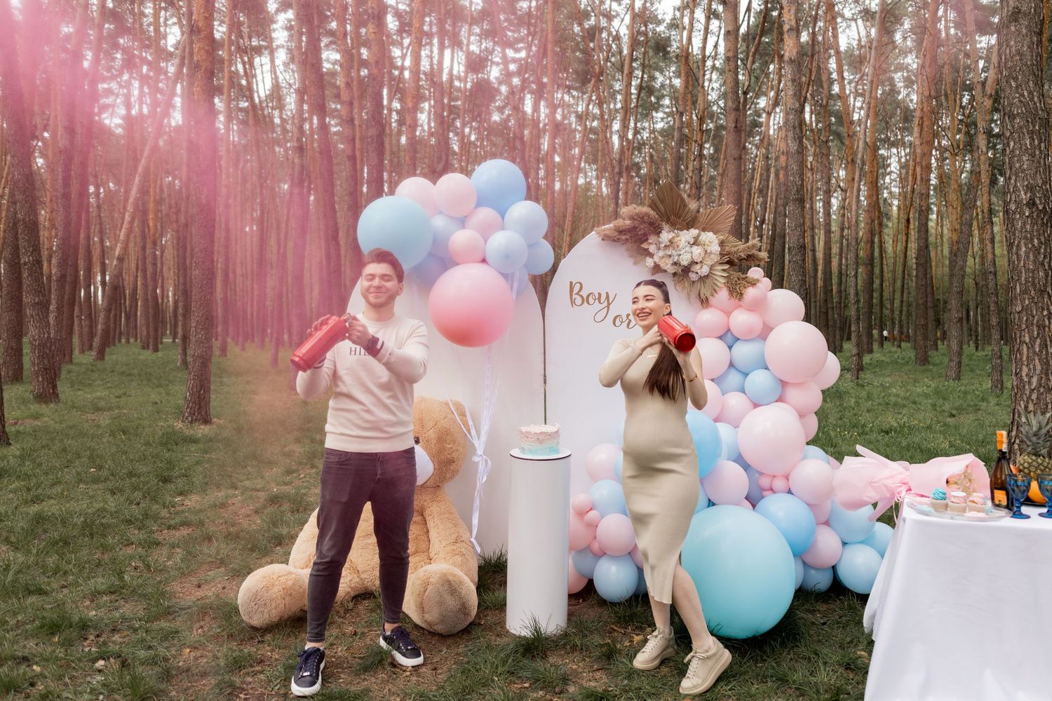 Pink smoke announcement at outdoor gender reveal party with balloon decorations.