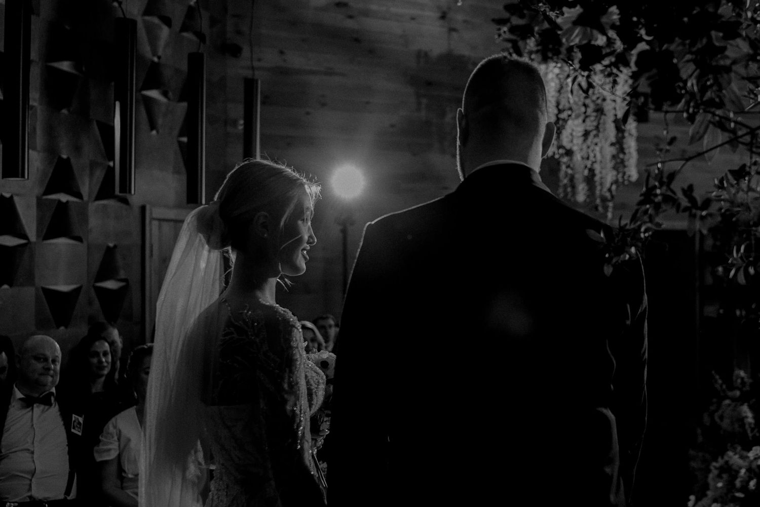 Black and white photo of bride and groom standing at wedding altar with soft light glowing behind them.