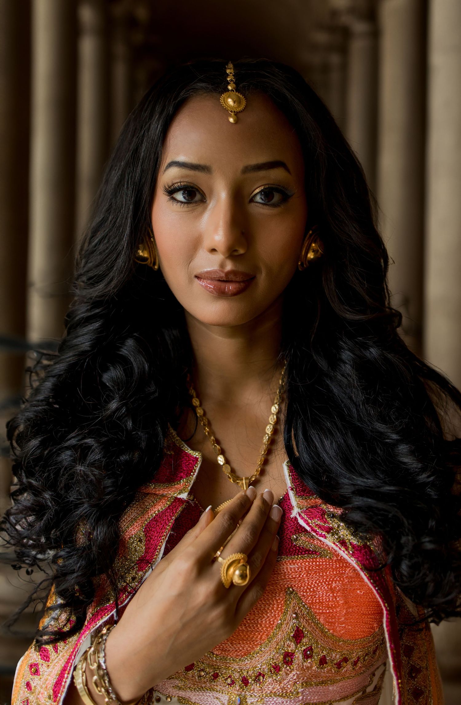Woman in traditional South Asian attire with gold jewelry, maang tikka, and elegant wavy black hair.