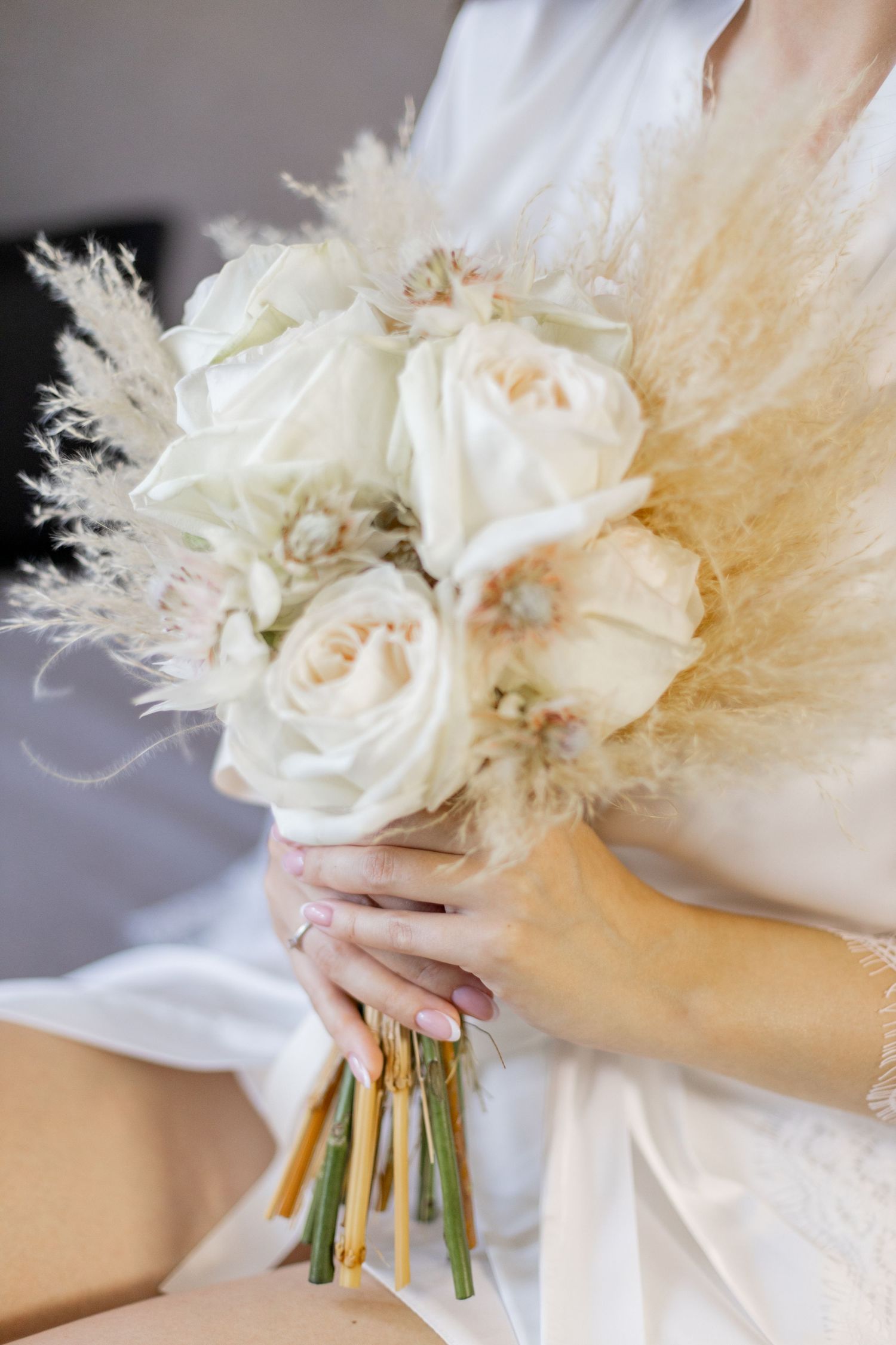 Elegant bridal bouquet featuring white roses and dried pampas grass wrapped with ribbon.