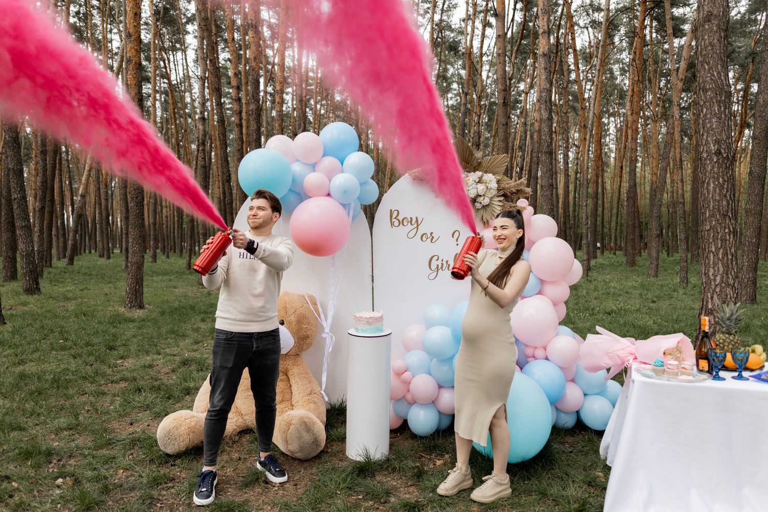 Pink smoke effect during gender reveal celebration in forest with balloon decorations.