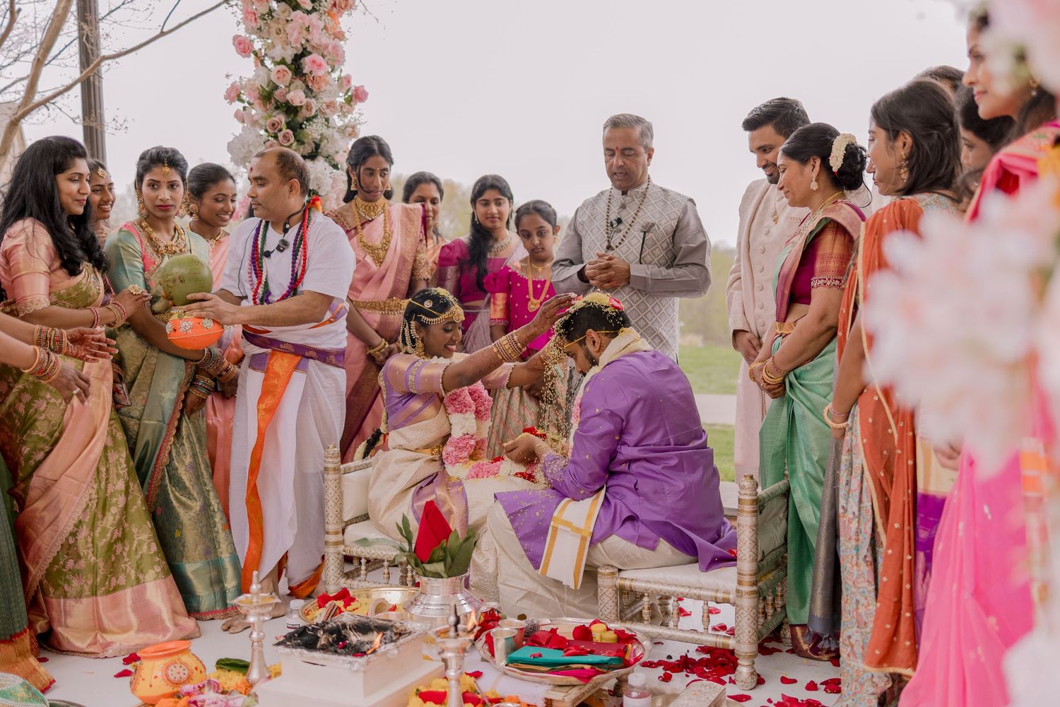 Colorful Indian wedding ceremony outdoors with guests in vibrant saris surrounding couple during traditional rituals.