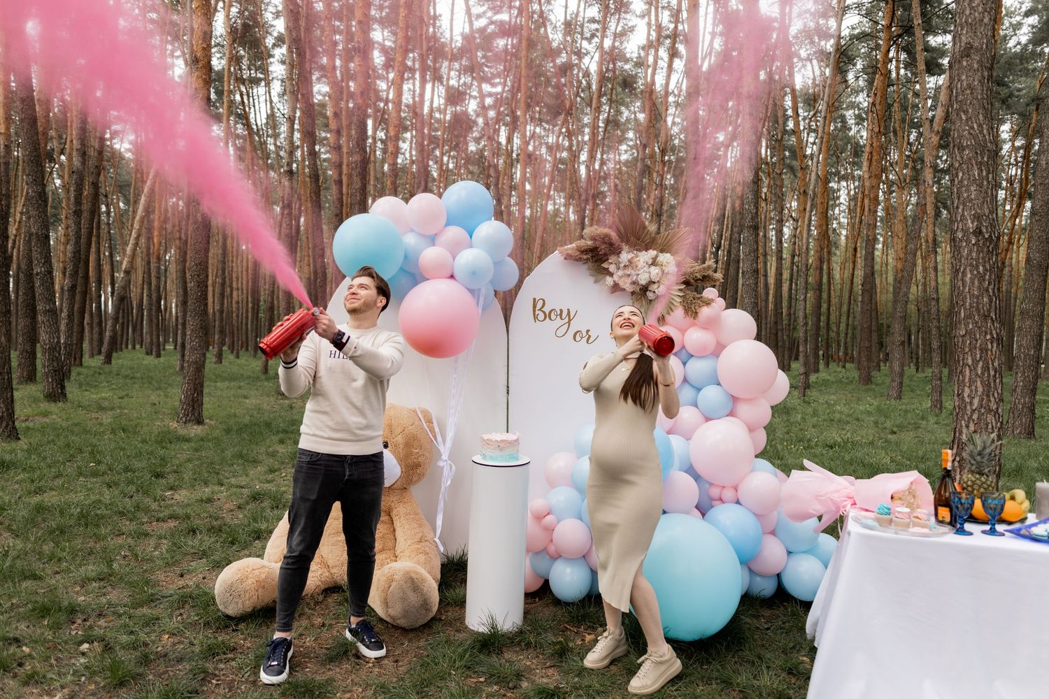 Forest gender reveal party scene with pink smoke and decorative balloon arrangements.