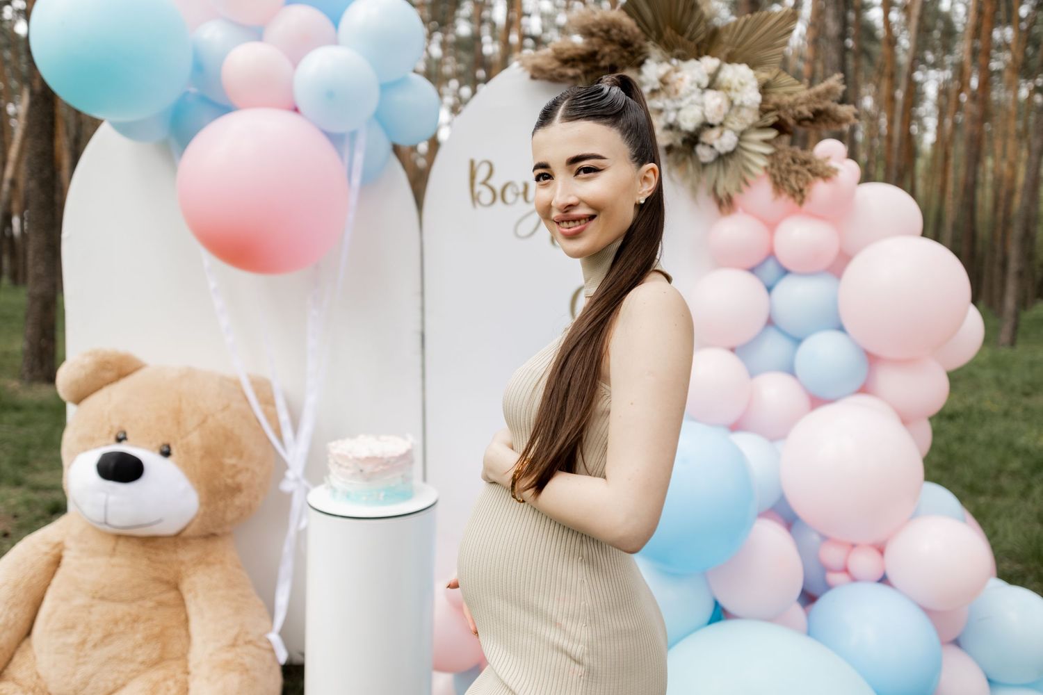 Pink and blue balloon arrangement with decorative elements for gender reveal party in forest.