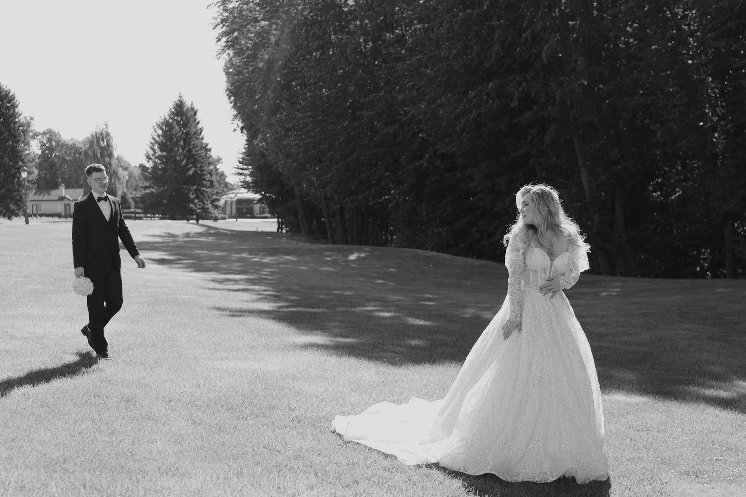 Black and white photo of a bride in a flowing gown and groom in a suit on a lush green lawn.