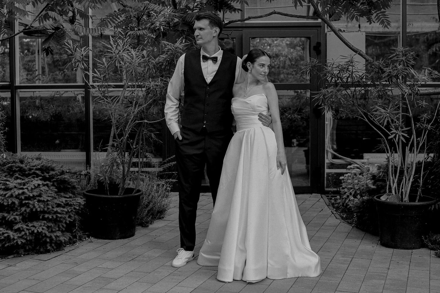 Black and white photo of a bride and groom posing outdoors near lush greenery on their wedding day.