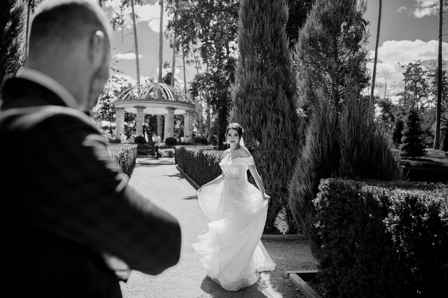 Black and white photo of a bride in a white gown twirling toward a groom in a garden wedding venue.