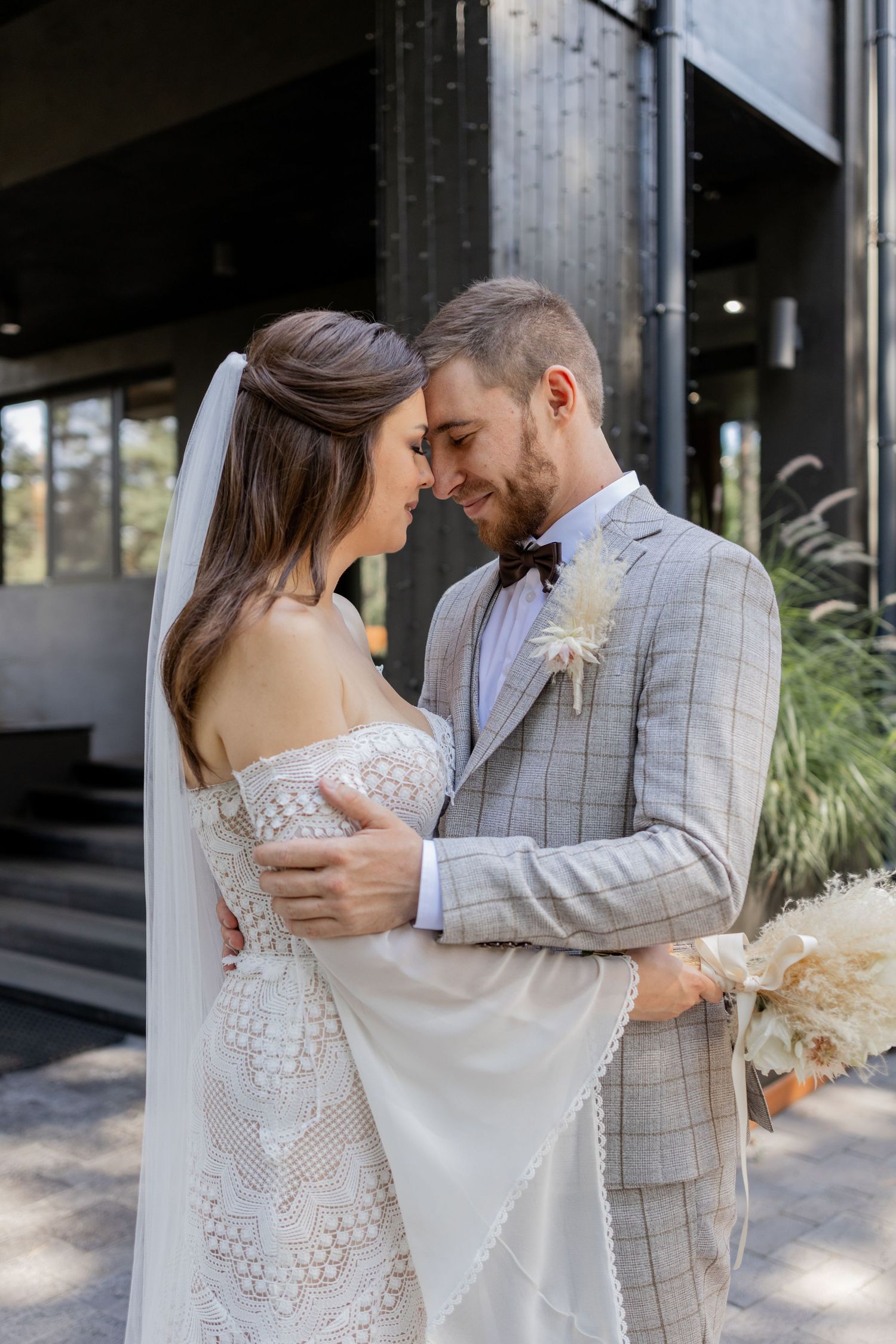 Tender moments between newlyweds against a modern building exterior with natural lighting.