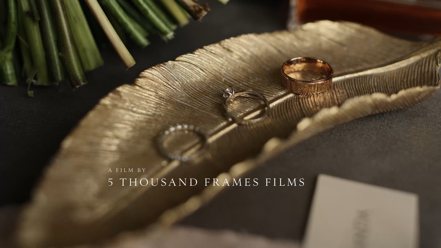Gold wedding bands and diamond engagement ring displayed on a decorative leaf dish by 5 Thousand Frames Films.