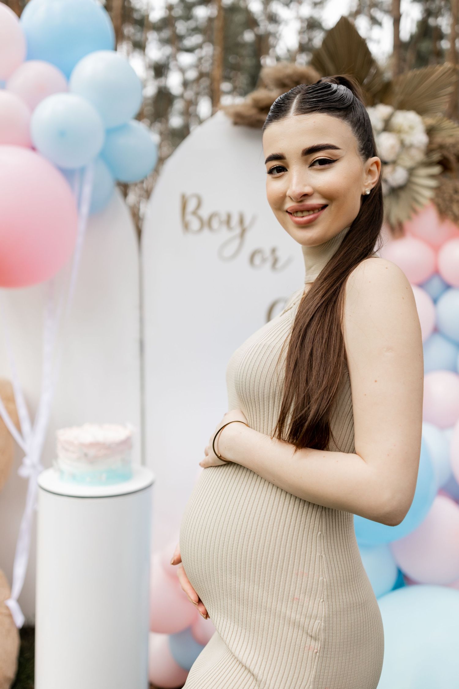 Festive gender reveal setup with balloon arch and decorative elements in natural forest setting.