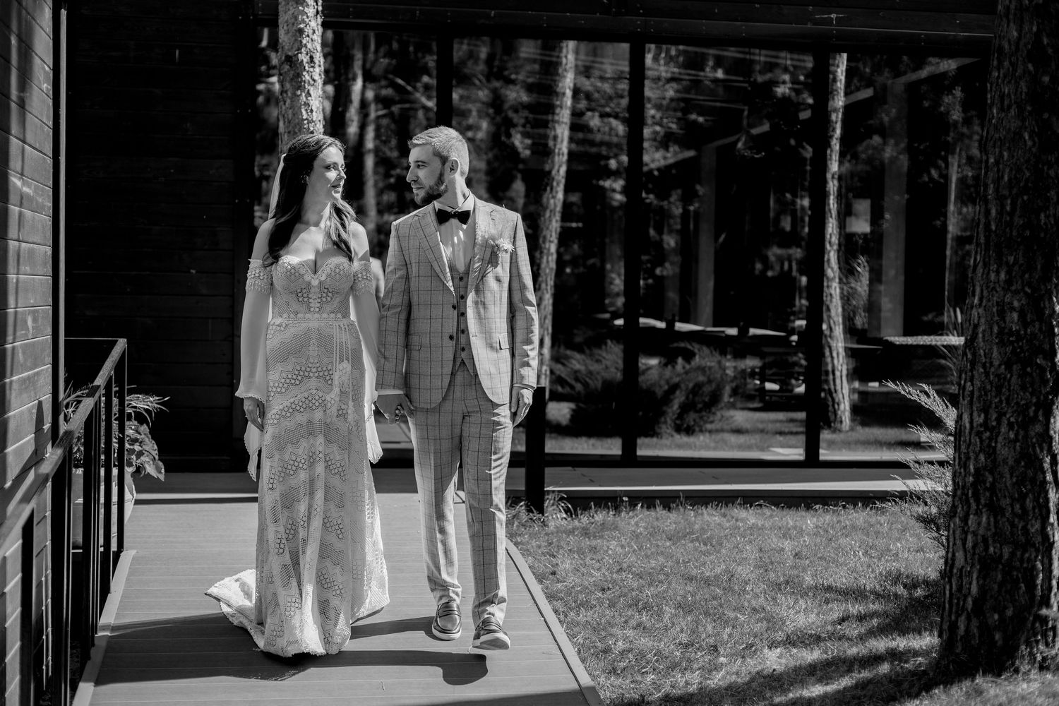 Wedding couple walks hand in hand through a wooded outdoor setting.