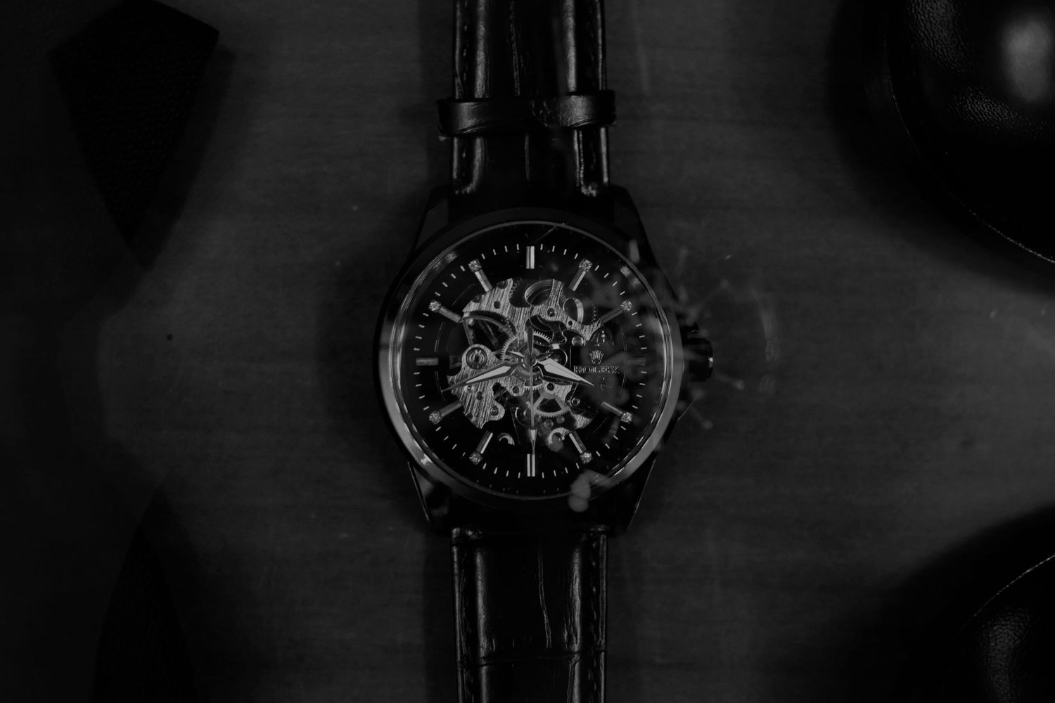 Black and white photo of a skeleton mechanical watch with leather strap on a dark wooden surface.