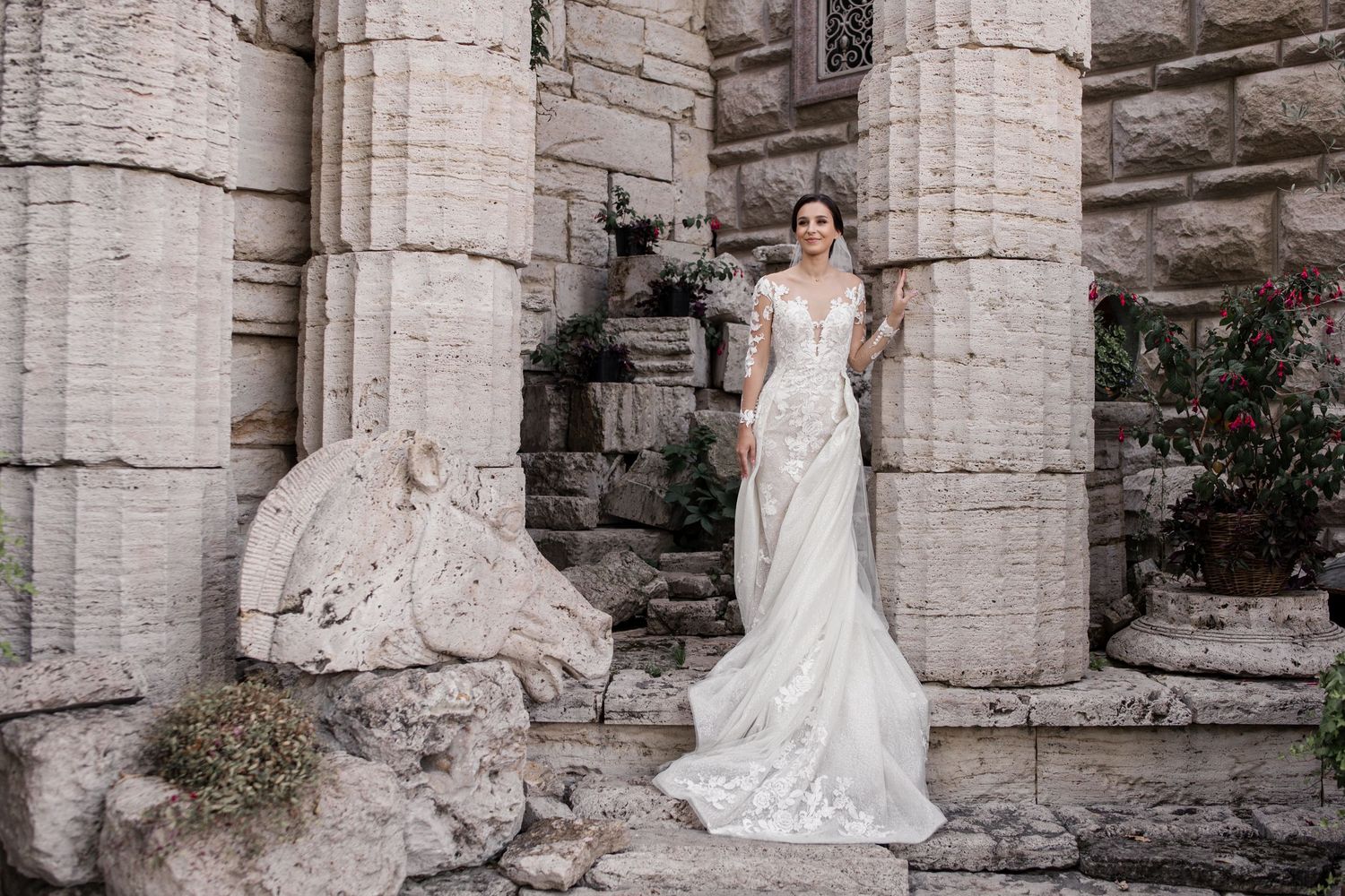 Bride in elegant lace wedding gown posing among ancient stone columns in a historic architectural setting.
