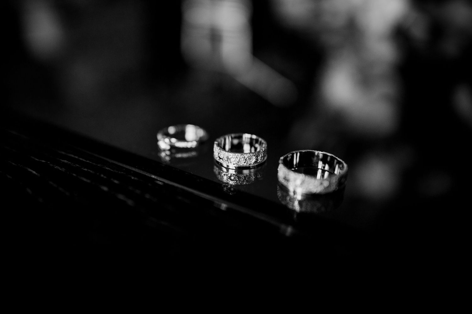 Black and white photo of three elegant diamond wedding rings displayed on a dark reflective surface.