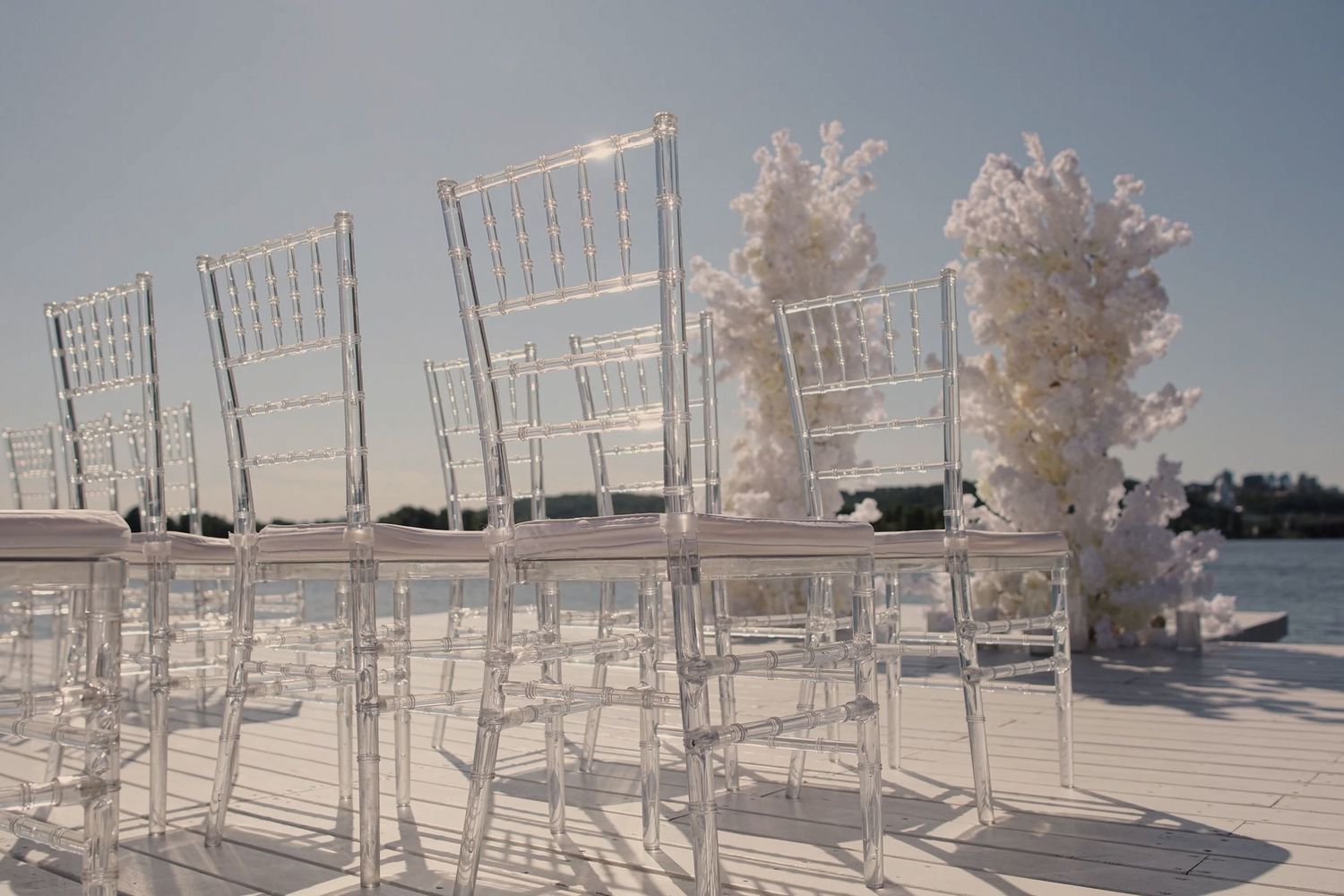 Clear acrylic Chiavari chairs arranged in rows at an elegant outdoor wedding ceremony venue with white floral decor.