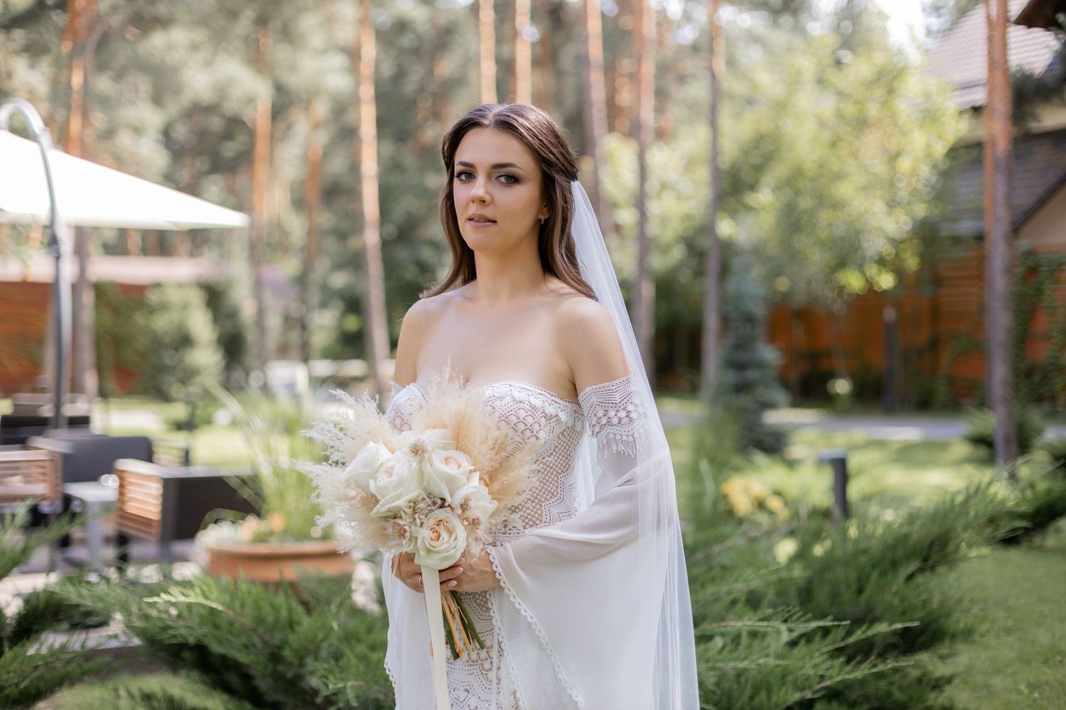 Elegant bride holds dried flower bouquet in outdoor garden setting.