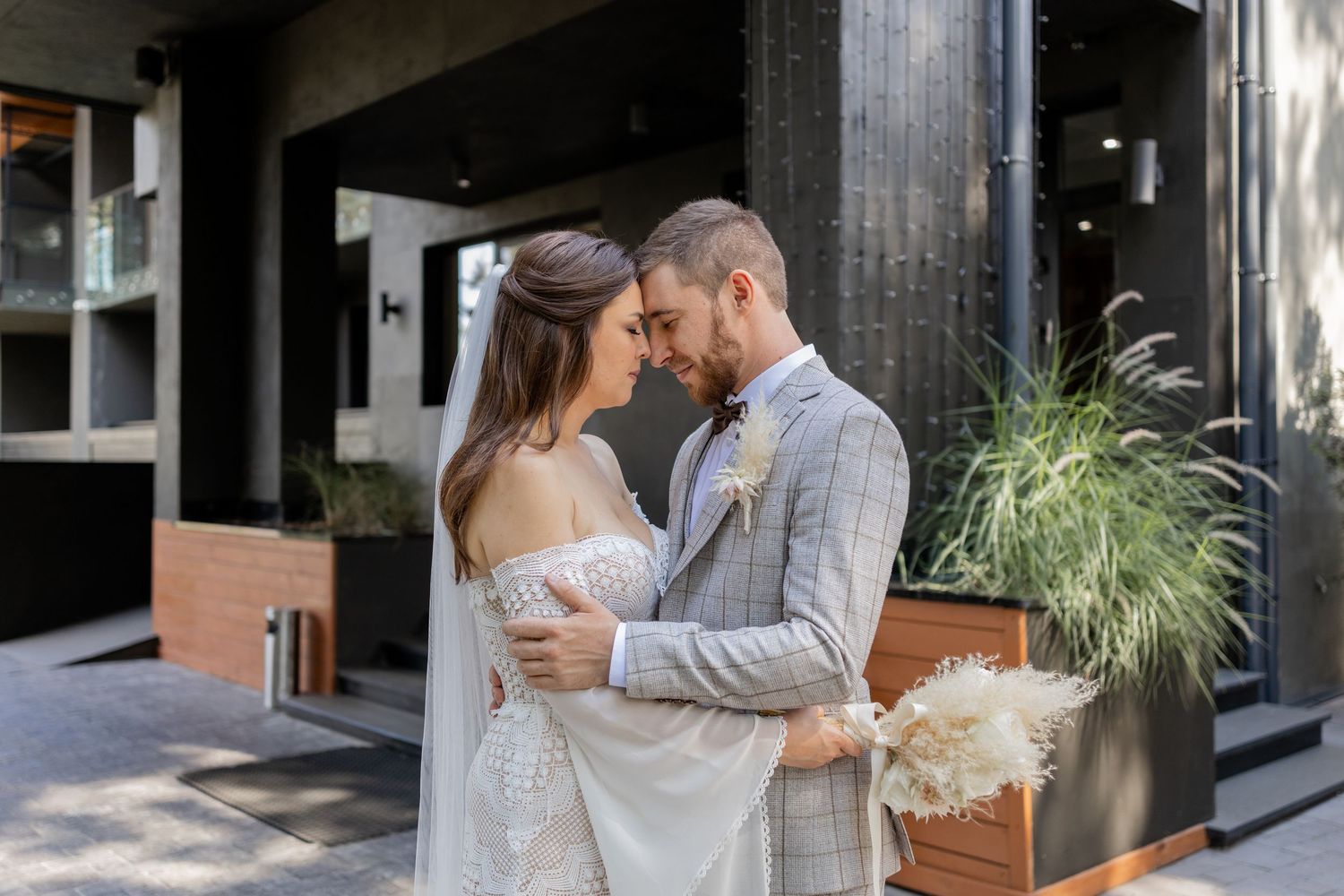 Intimate wedding portraits against industrial-modern architecture with decorative plants.