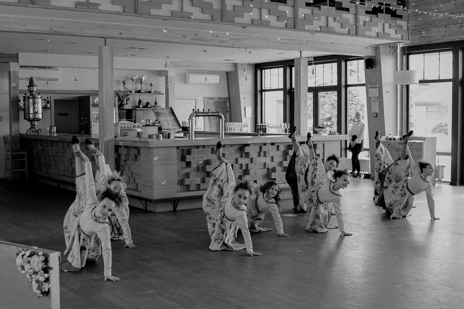 Children perform a traditional dance in costume inside a spacious hall, captured in black and white photography.