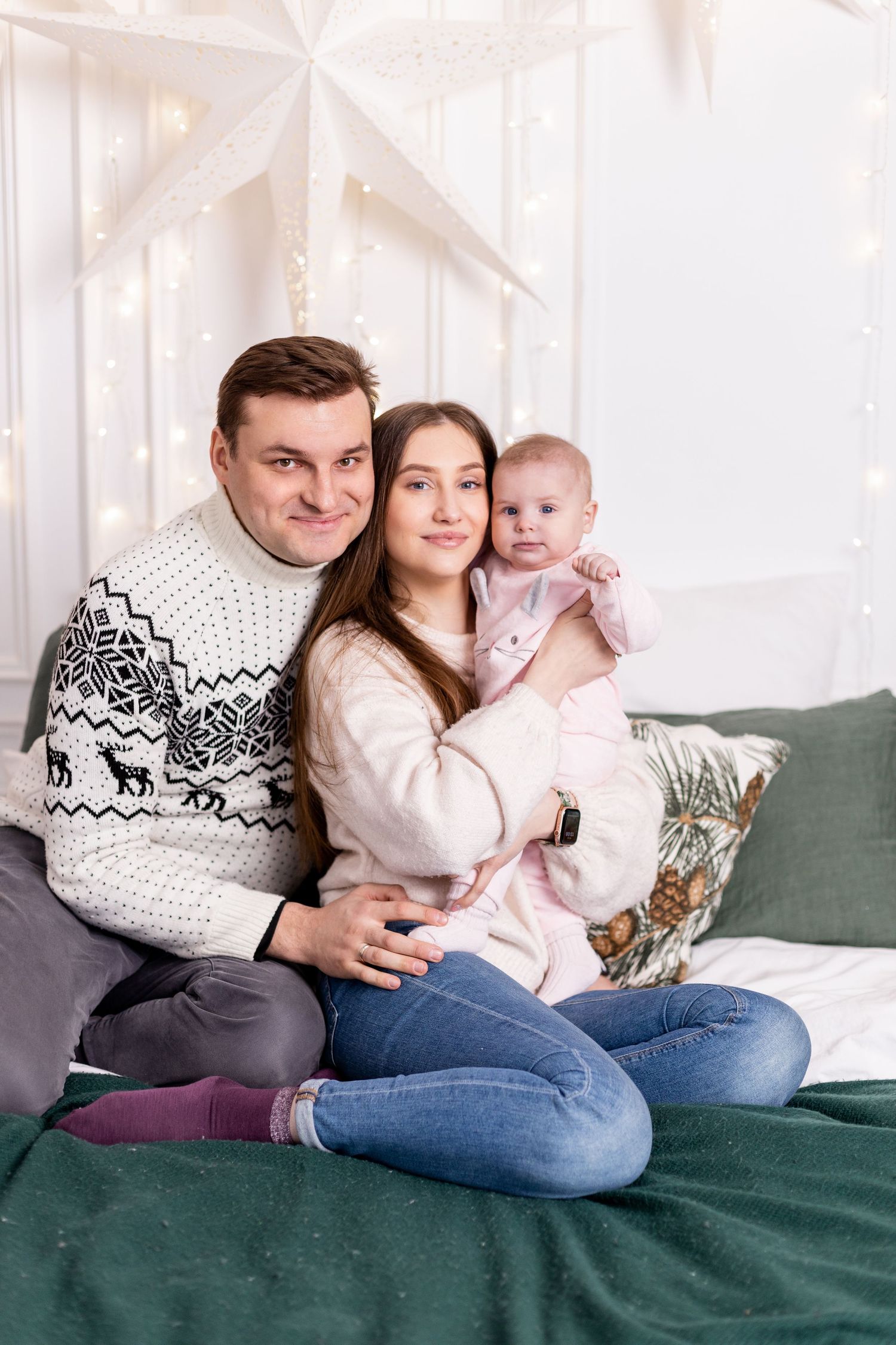 Family wearing matching winter sweaters cuddles together on a green couch during holiday season.
