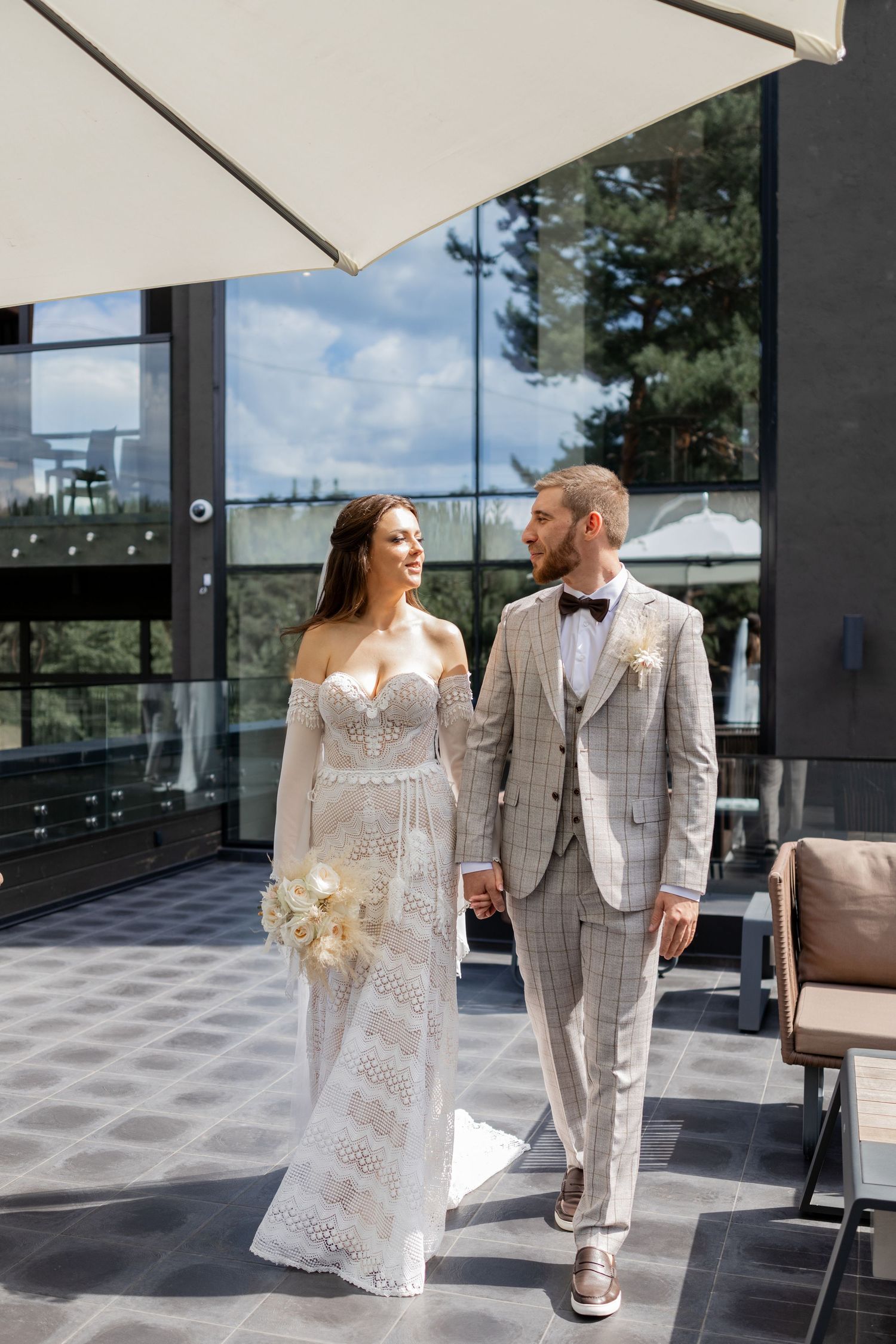 Wedding couple in white and plaid outfits pose together on a modern outdoor terrace.