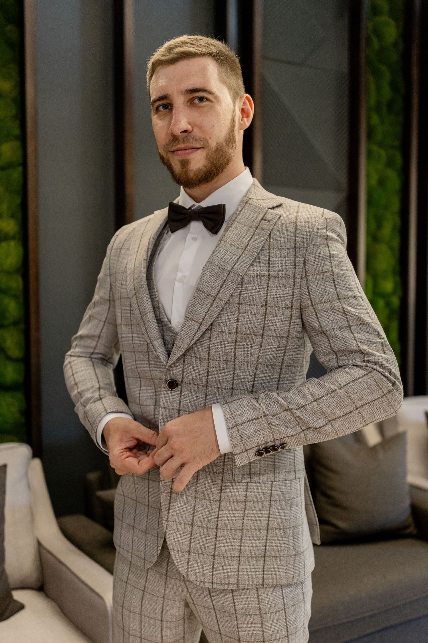 Sophisticated gray plaid suit styled with black bow tie in contemporary setting.