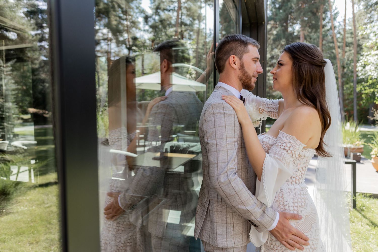 Newlyweds pose together against a backdrop of tall pine trees and glass walls.