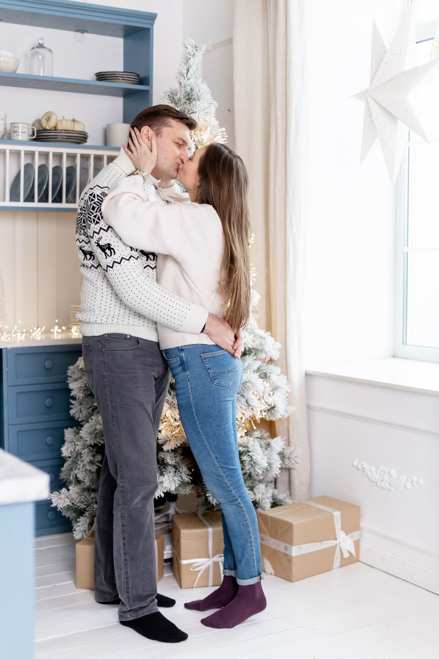 Intimate moment shared in a bright room with festive winter decorations and blue built-in shelves.
