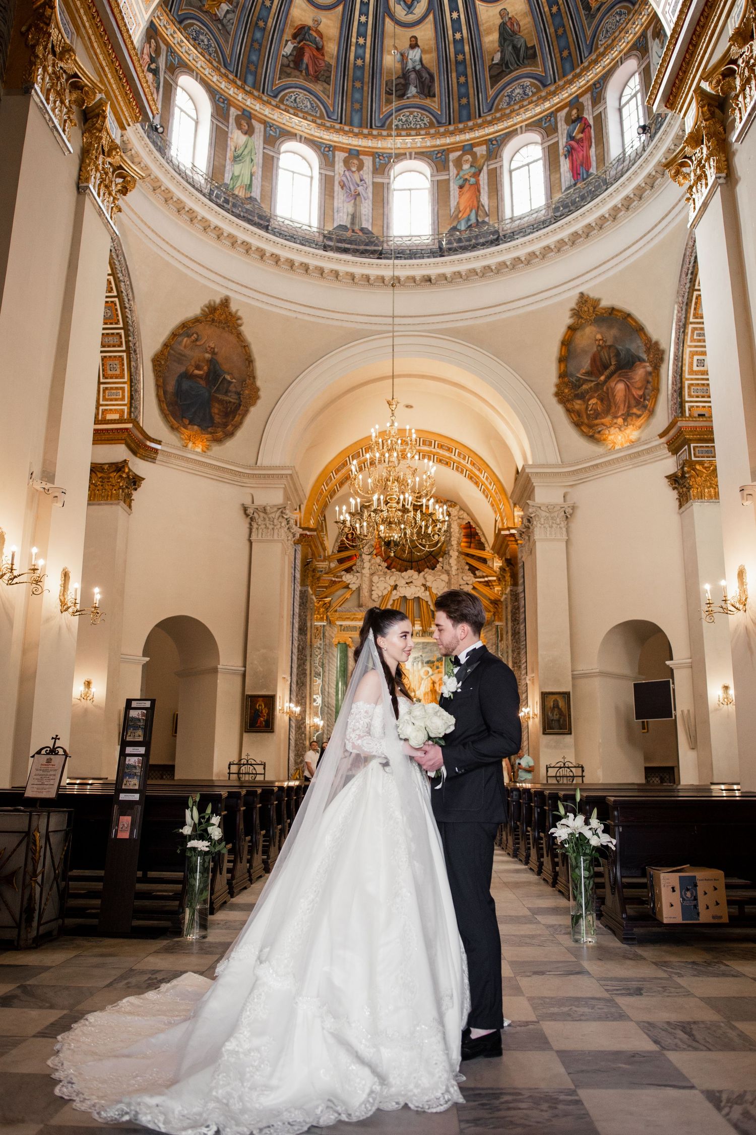 Bride and groom stand together in an ornate cathedral with a stunning domed ceiling, chandelier, and painted murals.