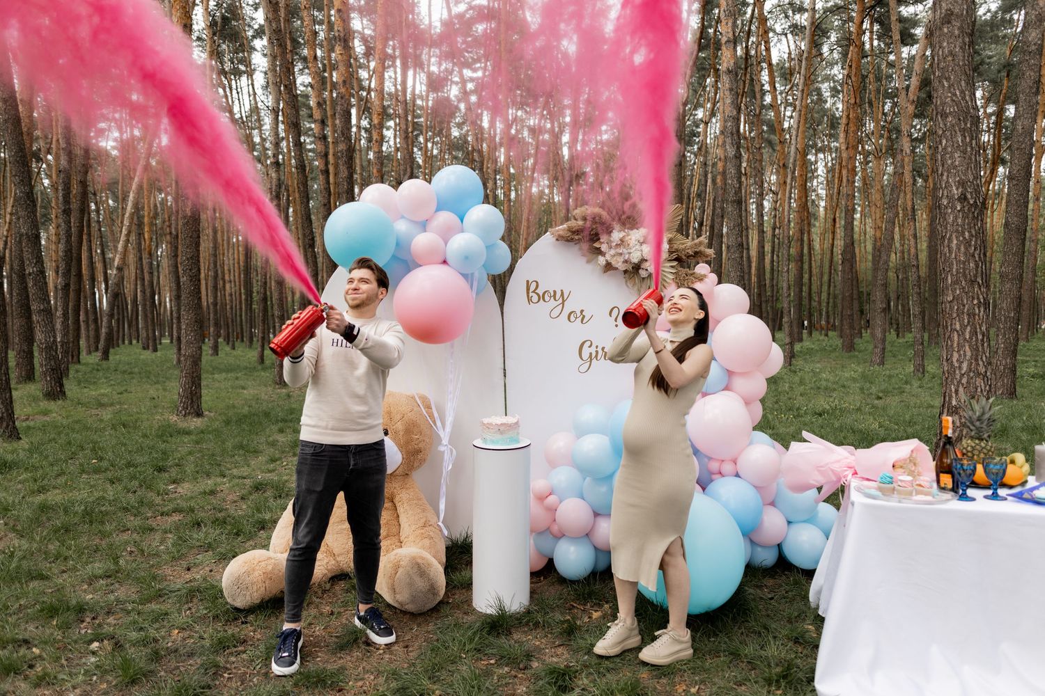 Pink smoke fills the air at outdoor gender reveal party with balloon arch and decorations.