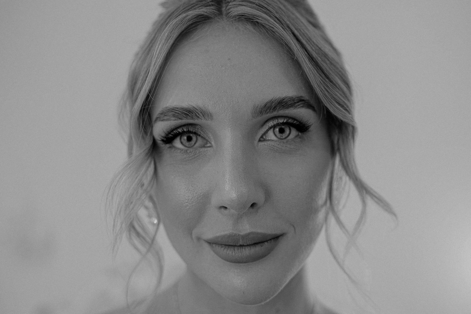 Close-up black and white portrait of a young woman with elegant updo hairstyle and long lashes.