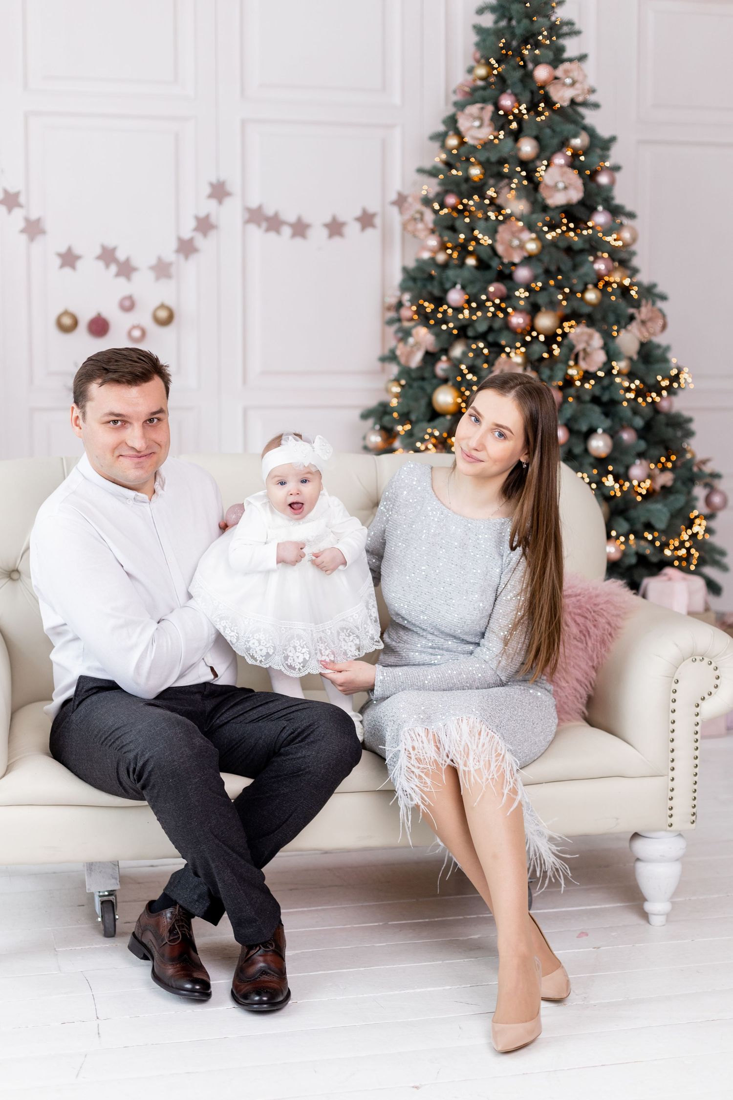 Family sharing playful moment on white couch near decorated Christmas tree.