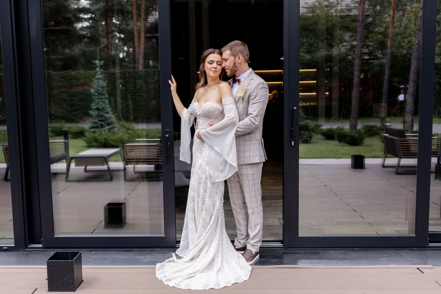 Wedding couple shares intimate moments in front of a contemporary glass building with forest backdrop.