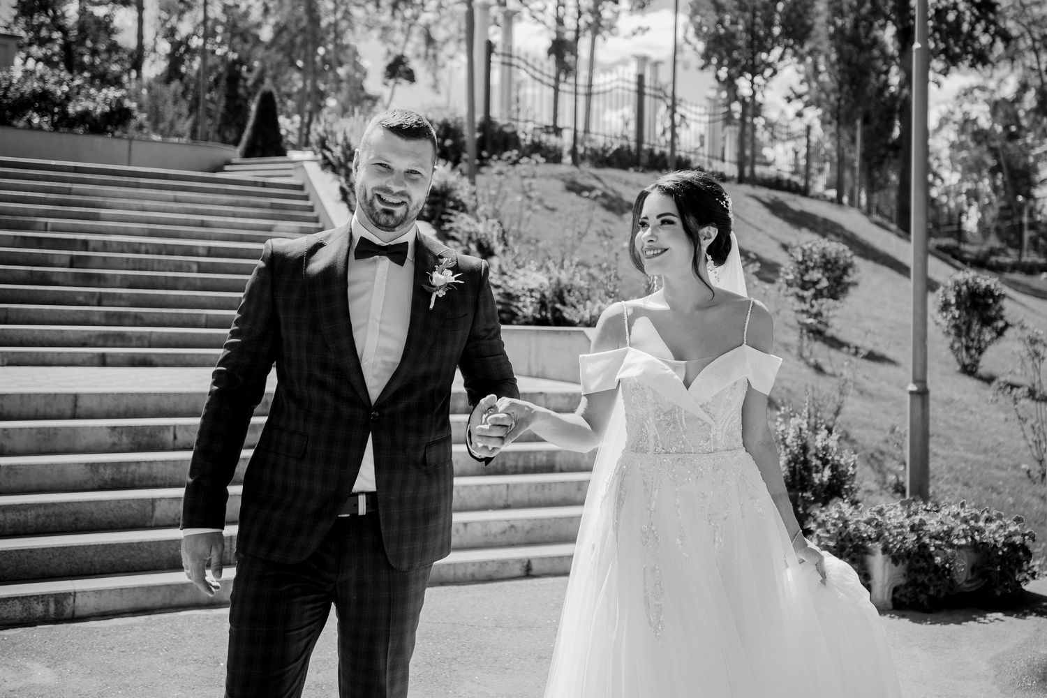 Black and white photo of a laughing bride and groom walking outdoors on their wedding day.