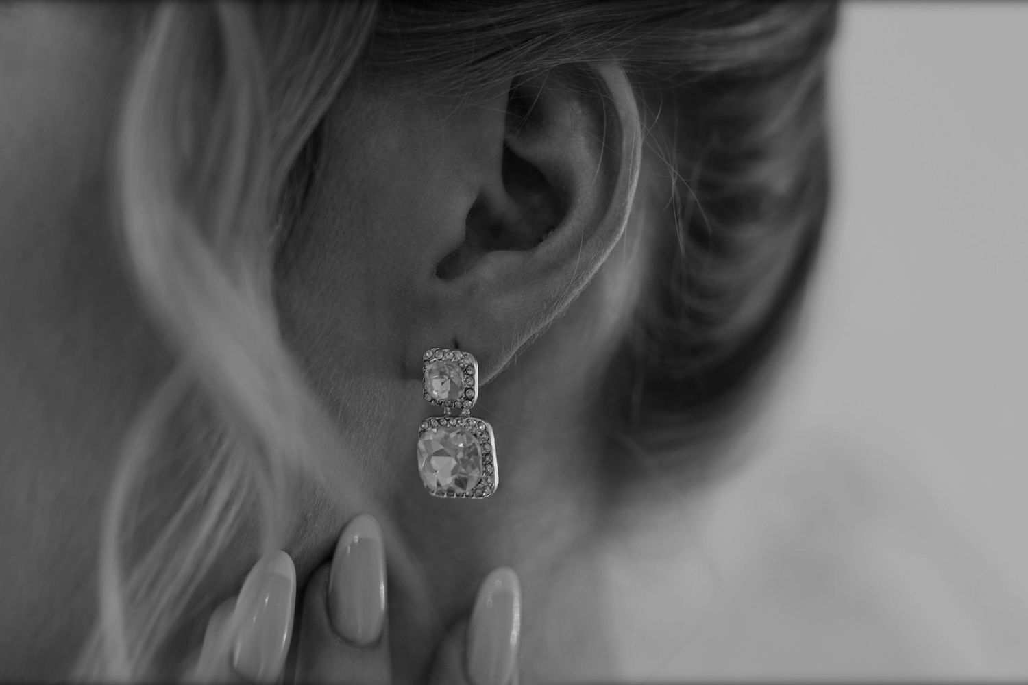Close-up of elegant diamond drop earrings on a woman with blonde updo hair, shown in black and white photography.