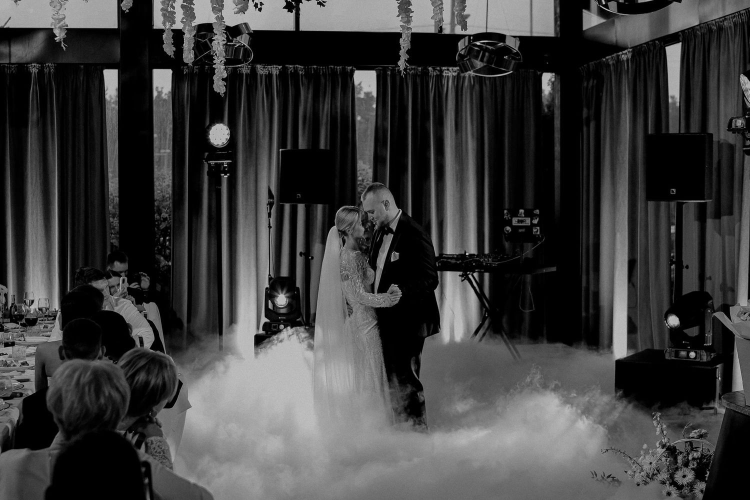 Black and white photo of a bride and groom sharing their first dance surrounded by dramatic fog at a wedding reception.