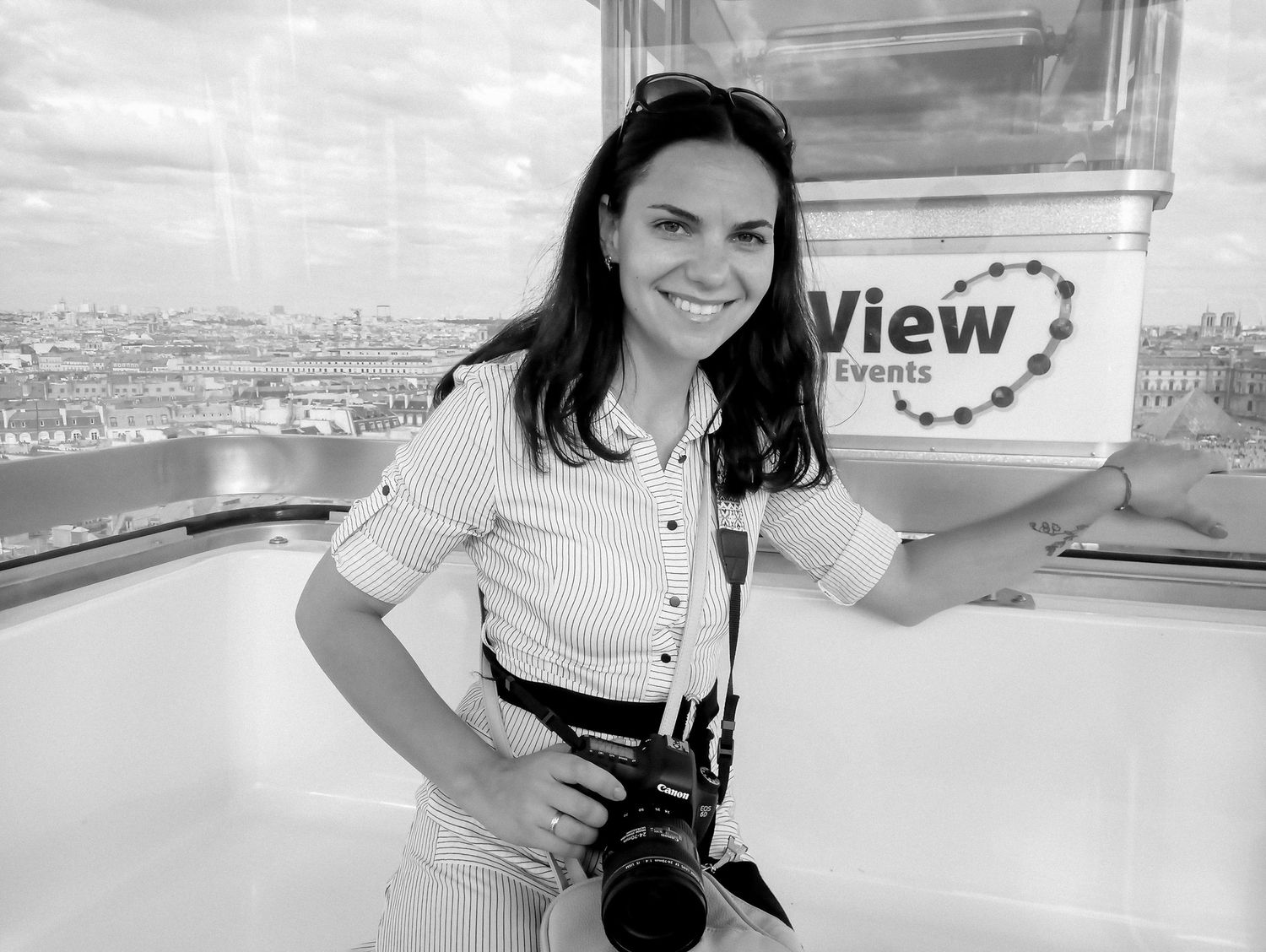 Woman with camera smiling at View Events venue with Paris cityscape in background, black and white photo.