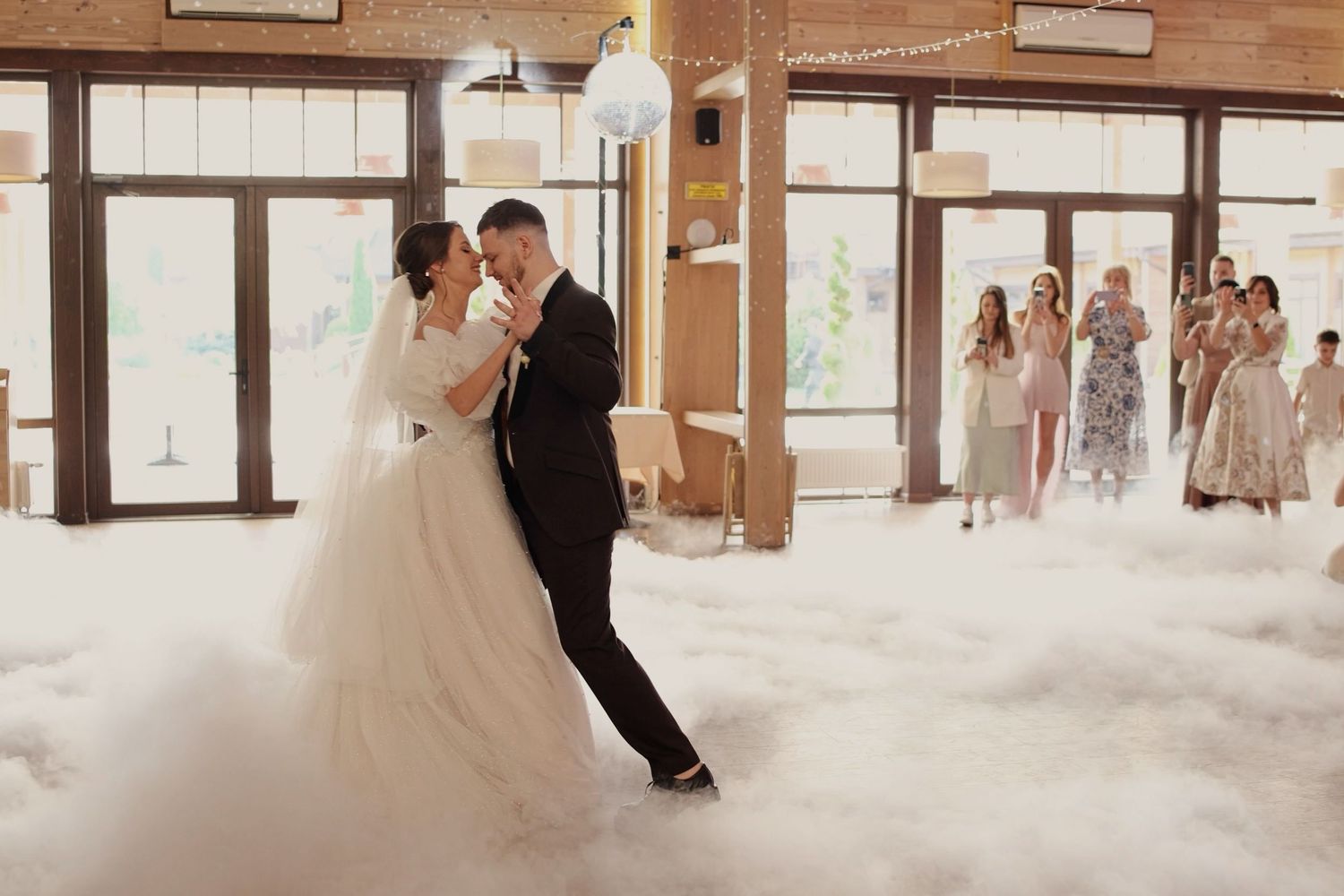 Bride and groom share first dance surrounded by romantic low fog at elegant wedding reception.