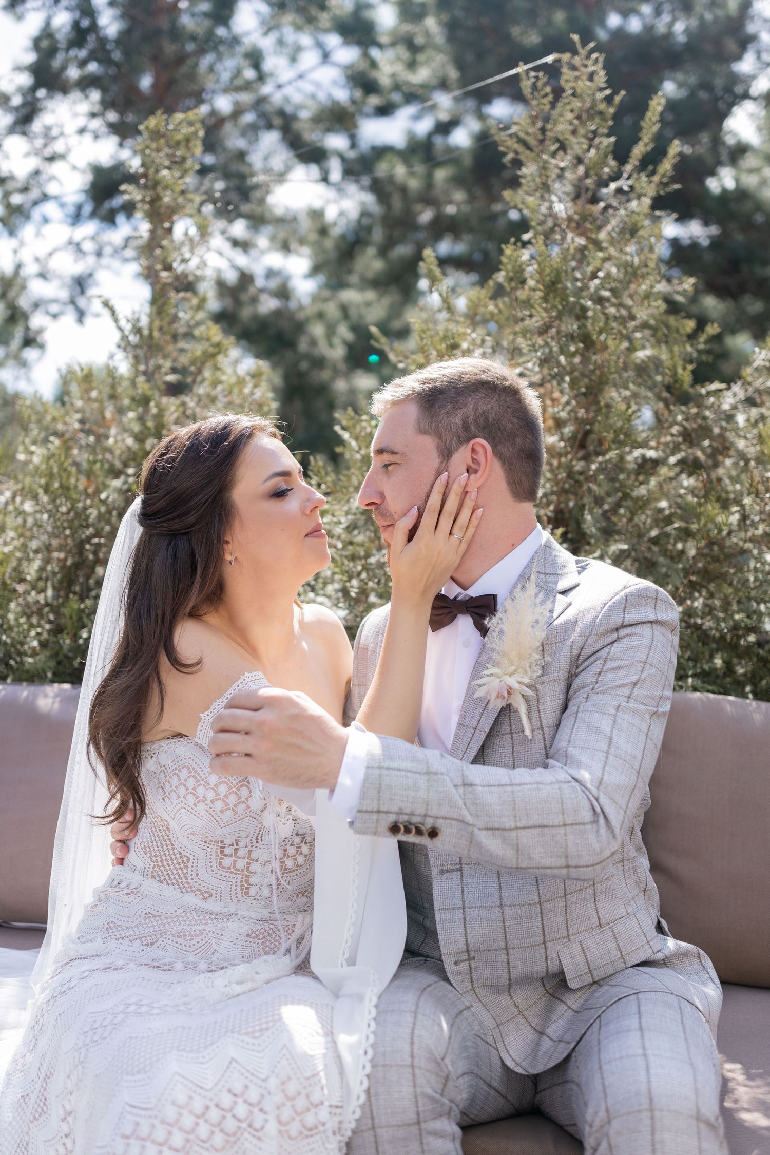 Wedding couple sharing tender moments on a brown bench in a natural outdoor setting.