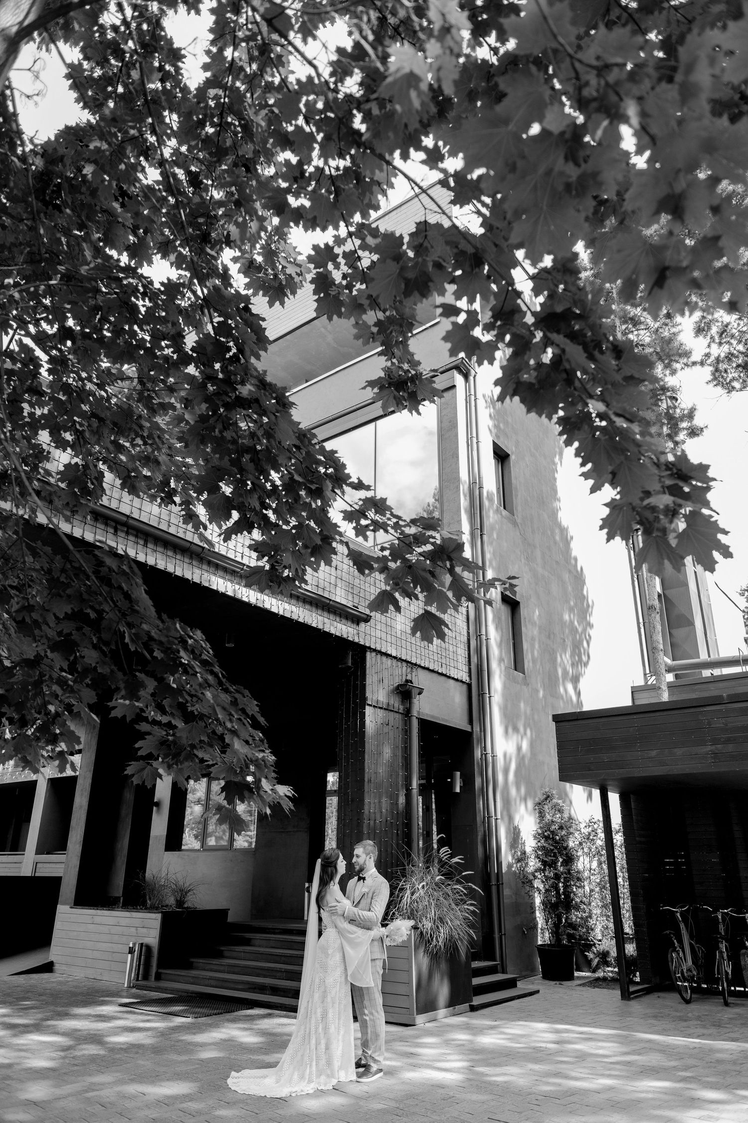 Black and white wedding photos captured against modern architectural backdrop with maple trees.