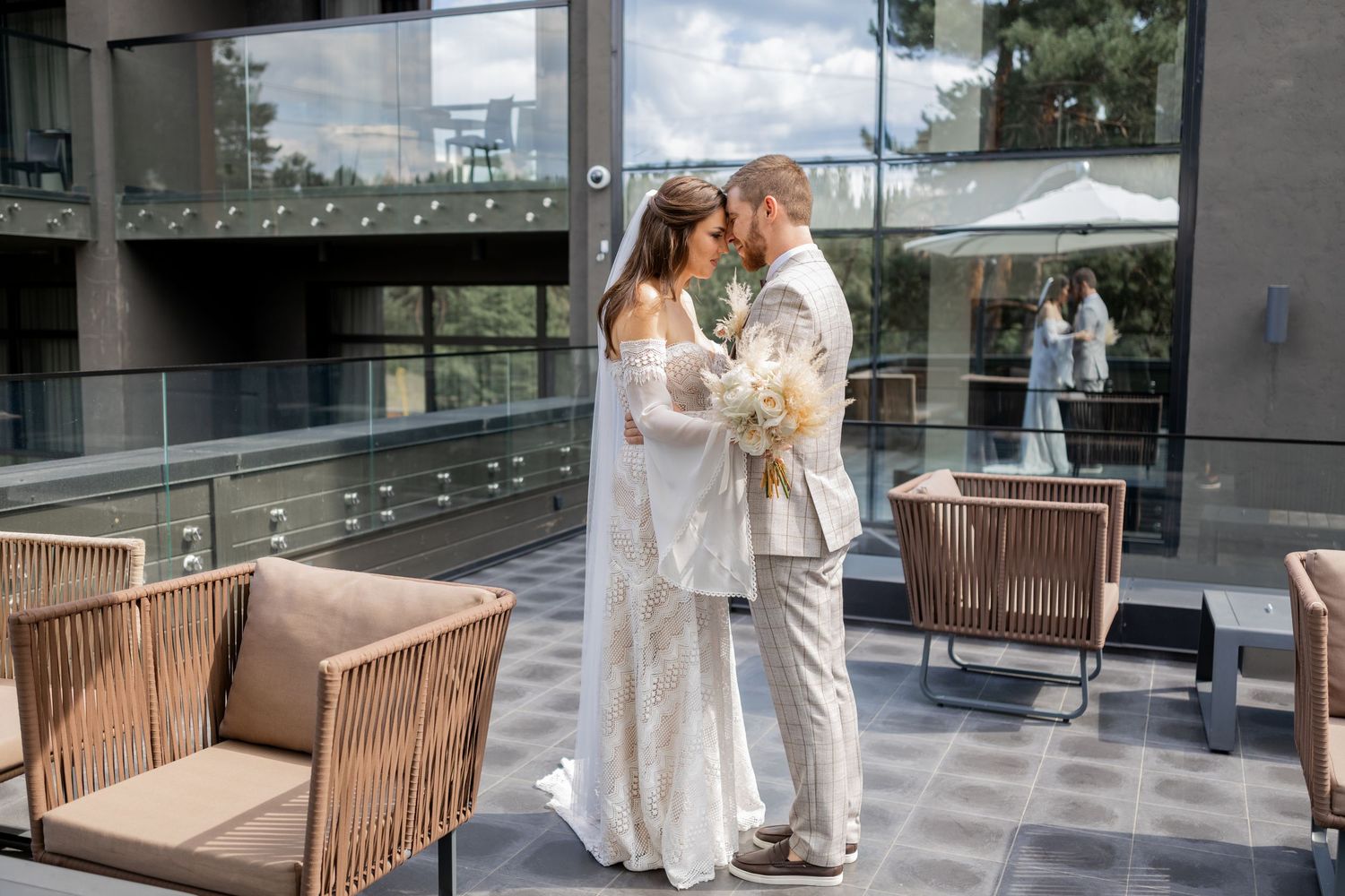 Panoramic view of a modern terrace with glass walls and wooden benches where a wedding moment unfolds.