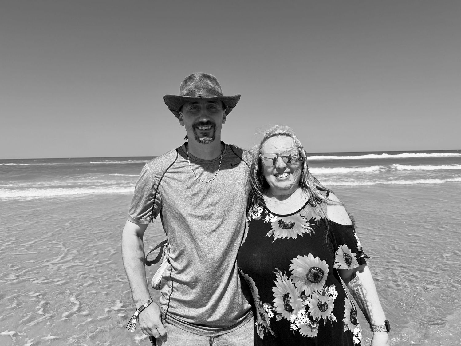 Happy couple enjoying a sunny day at the beach with waves and ocean in the background.