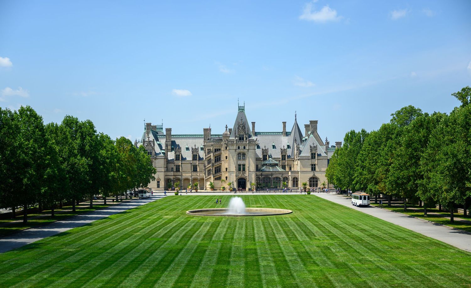 A panoramic view of a grand historic building with a perfectly manicured lawn and trees at Biltmore Estate.