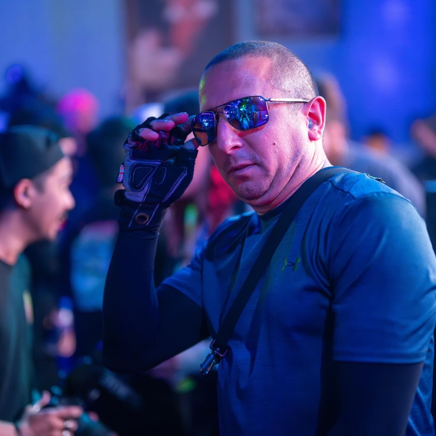 A security professional in a blue shirt and reflective sunglasses observes a crowd in a dimly lit environment.