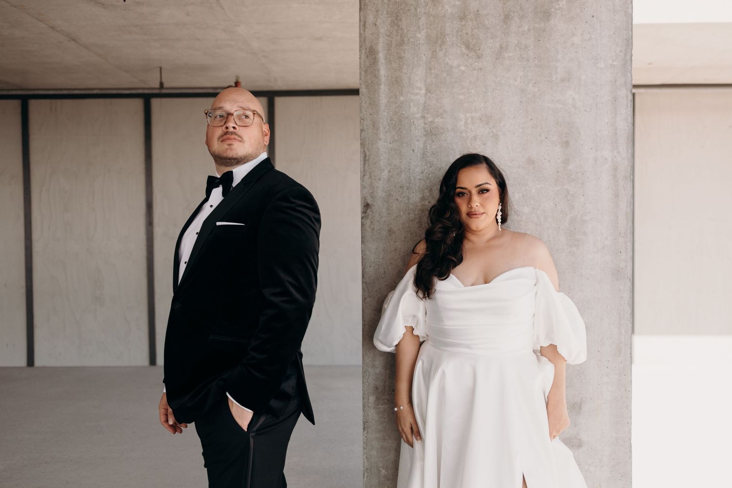 A couple in formal wedding attire pose in a modern concrete space with minimalist architecture.